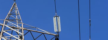 Symbolbild Energie: Teil eines Strommastes und Leitungen vor blauem Himmel