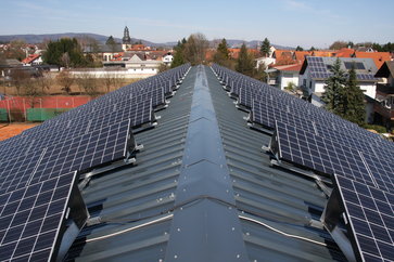 Dunkles Satteldach mit aufmontierter Photovoltaikanlage auf dem Sportzentrum Rimbach, im Hintergrund sieht man einige Wohnhäuser und die evangelische Kirche