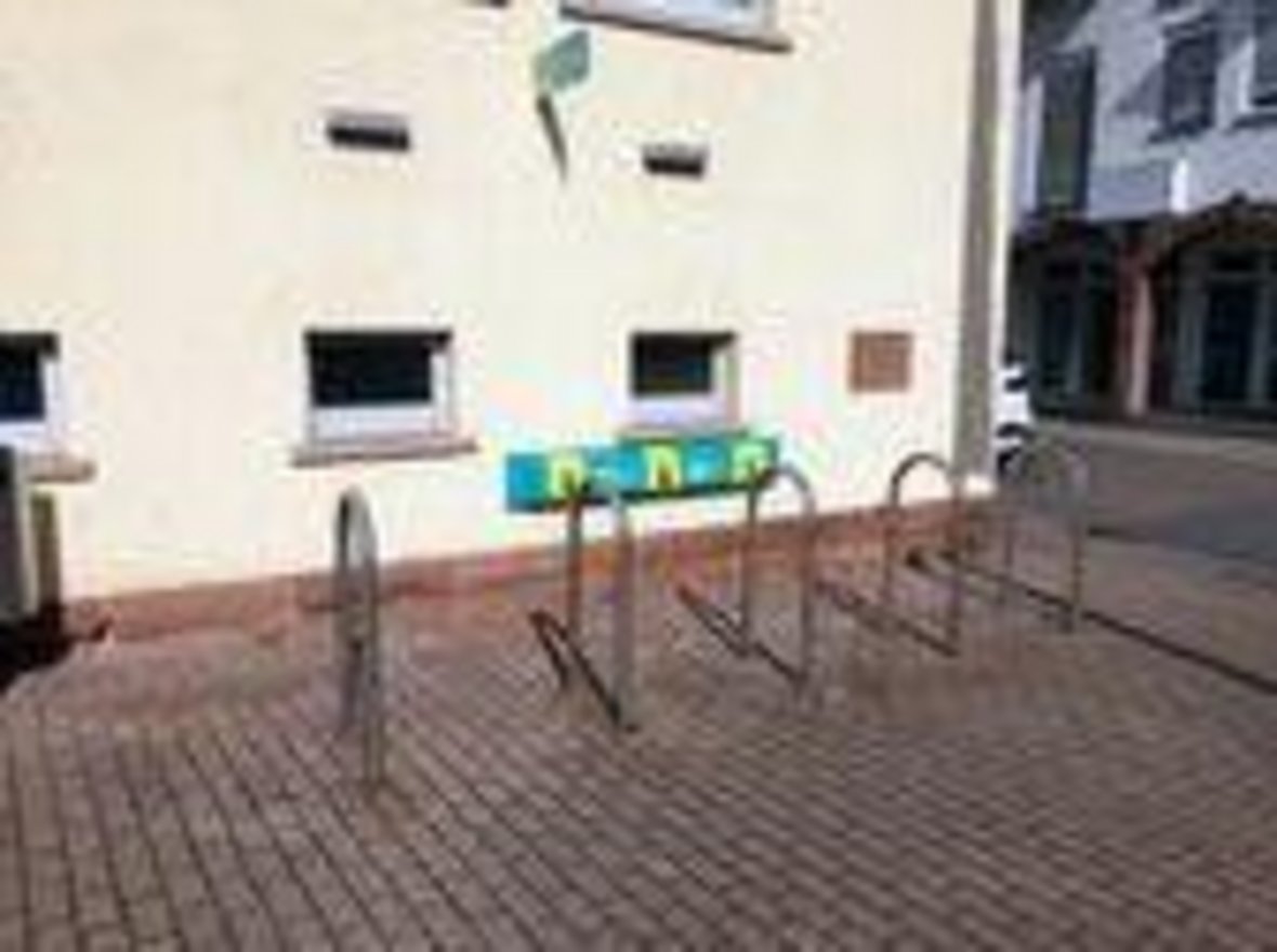 e-Bike Ladestelle am Rathaus, fünf Bügelfahrradständer, dahinter an der Rathauswand die Ladestadion mit drei Anschlüssen