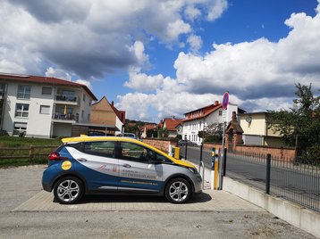 Standort Bismarckstraße, das Elektroauto der Gemeinde RImbach vor der LAdesäule, im Hintergrund sieht man die Löwenbrücke und Wohnbebauung