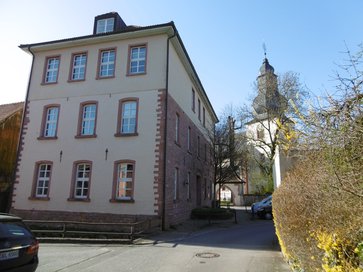 1877 errichtetes Volksschulgebäude, 1930 aufgestockt; im Hintergrund die Evangelische Kirche (Foto: Paul Kötter)